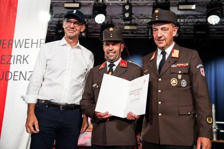 Bild: Landeshauptmann Markus Wallner, links, und Bezirksfeuerwehrinspektor Karl-Heinz Beiter, rechts, &uuml;berreichen Kommandant Xaver Stark, Mitte, das Feuerwehr-Verdienstkreuz in Bronze